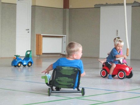 Zwei Kinder spielen in der Sporthalle mit ihren Fahrzeugen.
